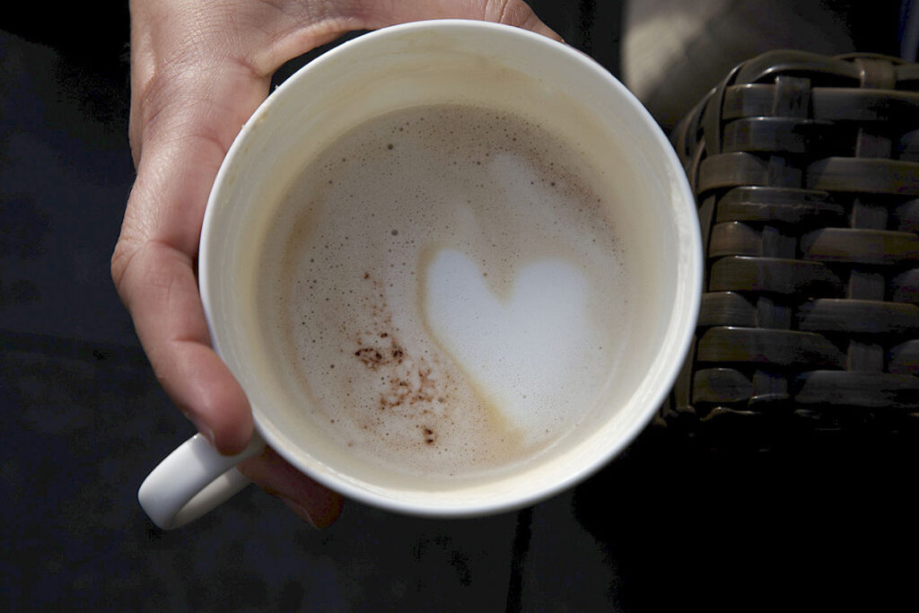 Une main tient une tasse à café dans laquelle la mousse de lait forme un coeur pendant l'apéro du mariage.