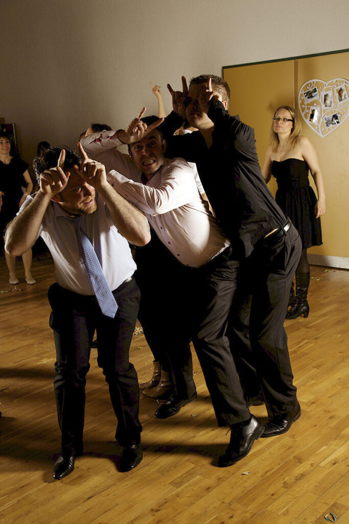 Trois hommes s'amusent sur la piste de danse de la fête de mariage en faisant les cornes et en accordéon.