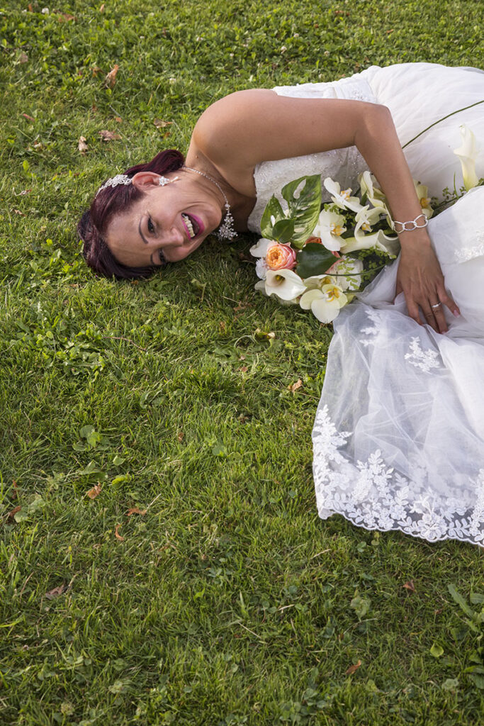 La mariée couchée sur le côté droite, en train de rire aux éclats dans le parc de l'hôtel du Léman à Chardonne.